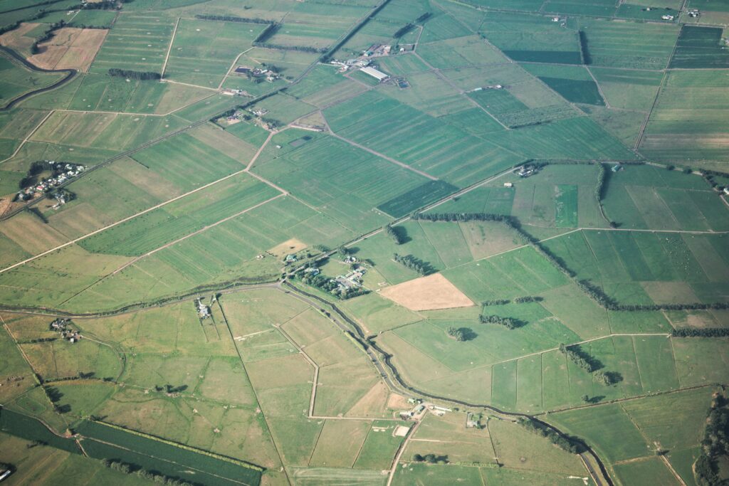 Expansive aerial view of green agricultural fields with scattered farmhouses and winding pathways.