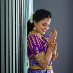 A beautiful Indian woman in a traditional saree adorned with gold jewelry, smiling gracefully indoors.